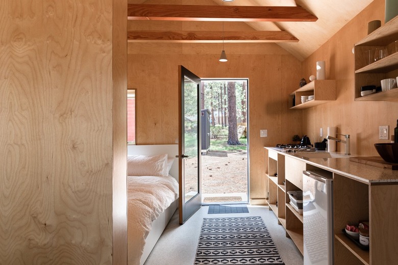 A wood cabin in the forest with a minimalist bedroom and wood walls and shelving