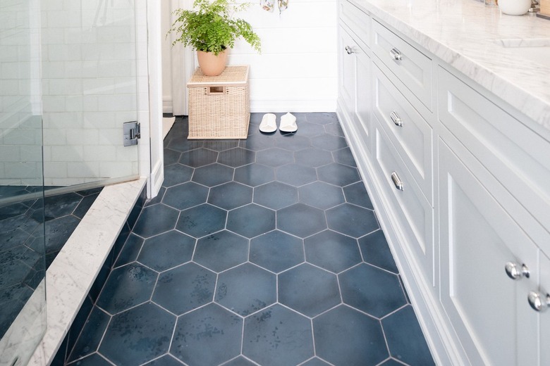 A small bathroom with white cabinets and a dark blue hexagonal tile floor.