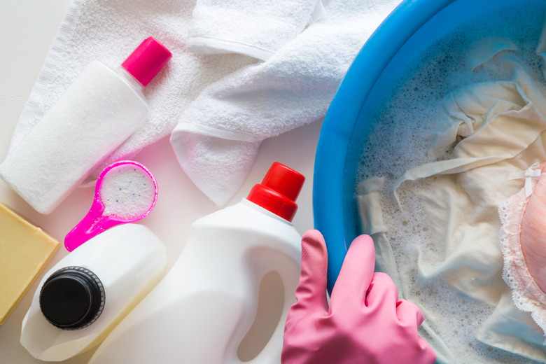 Housewife with rubber protective gloves washing clothes with different detergents in the bowl. Dry cleaning concept. Clothes care. Chores of maid. Regular washing.