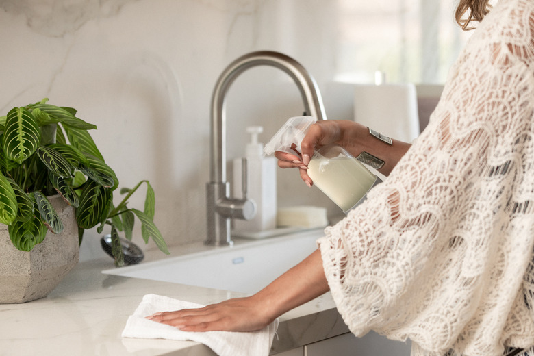 woman cleaning kitchen counter with spray and towel