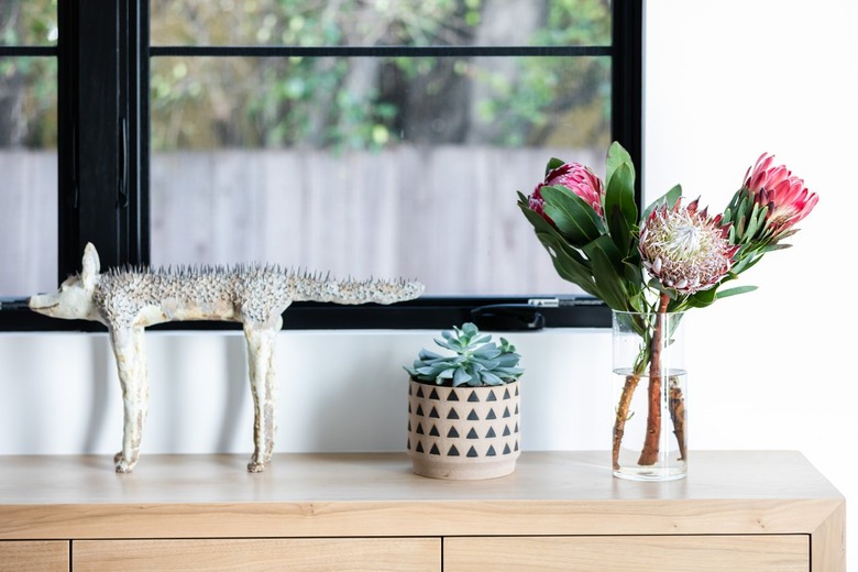 A wood sideboard with a sculpture, plant in a vase and vase of pink flowers