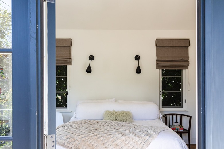 A bedroom with two windows covered with shades