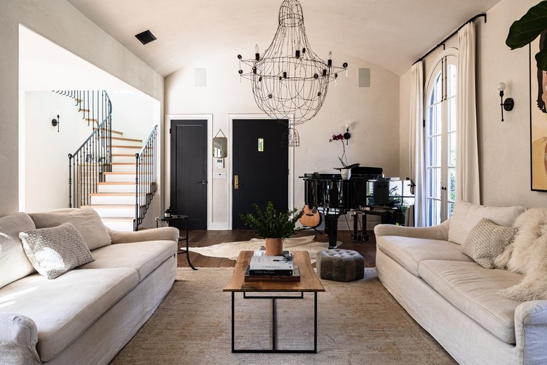 A white walled living room with white furniture, grand piano and chandelier