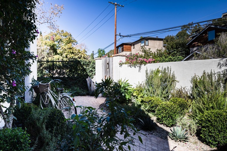 A back courtyard with two flowerbeds filled with green plants; a white concrete fence in a Spanish style surrounds the garden