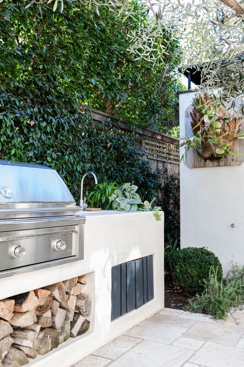 An outdoor patio grill with firewood and a sink with plants