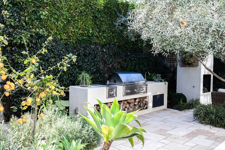 A grill with firewood surrounded by plants and trees on a patio