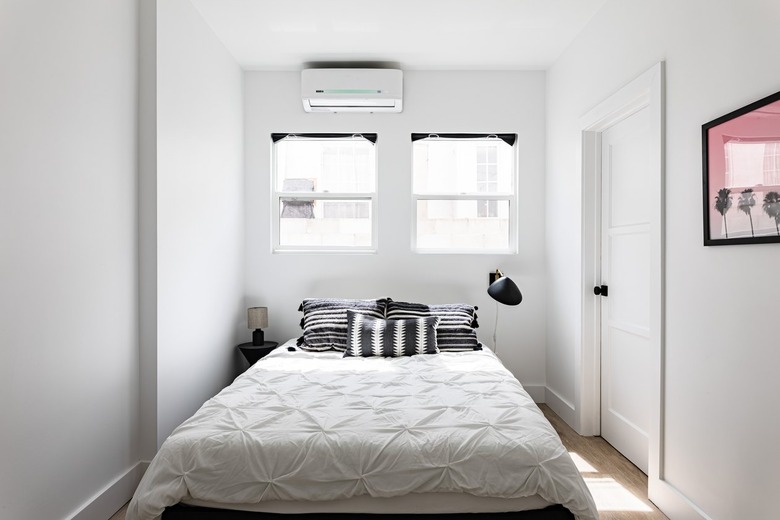 Ductless minisplit air conditioner in a minimalist white walled bedroom with white bedding and black accents