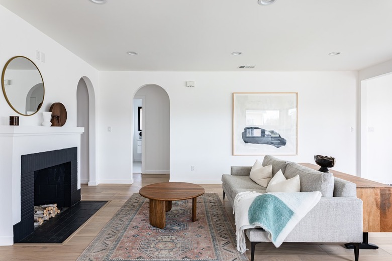 Contemporary living room with black fireplace, alcove with plants, green couch, hexagonal ottoman, and archway leading to hallway