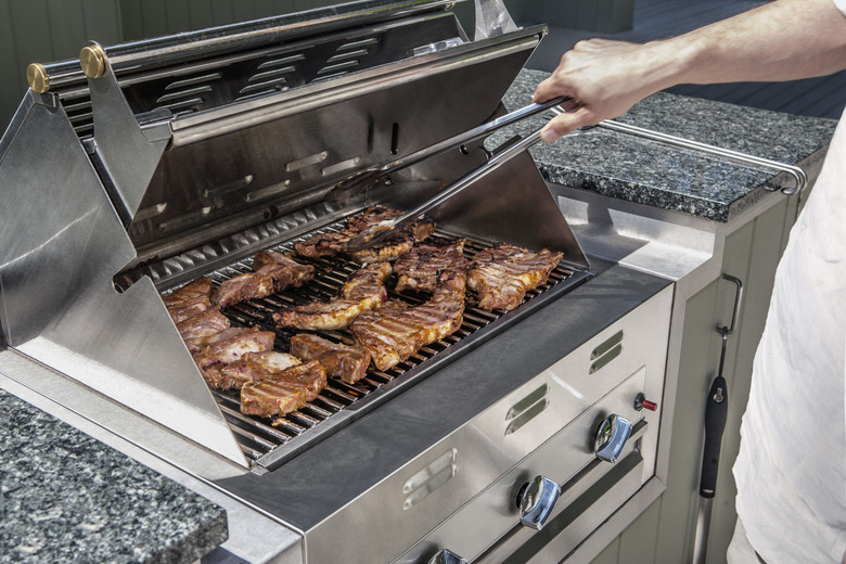 Turning steaks on outdoor propane gas grill.