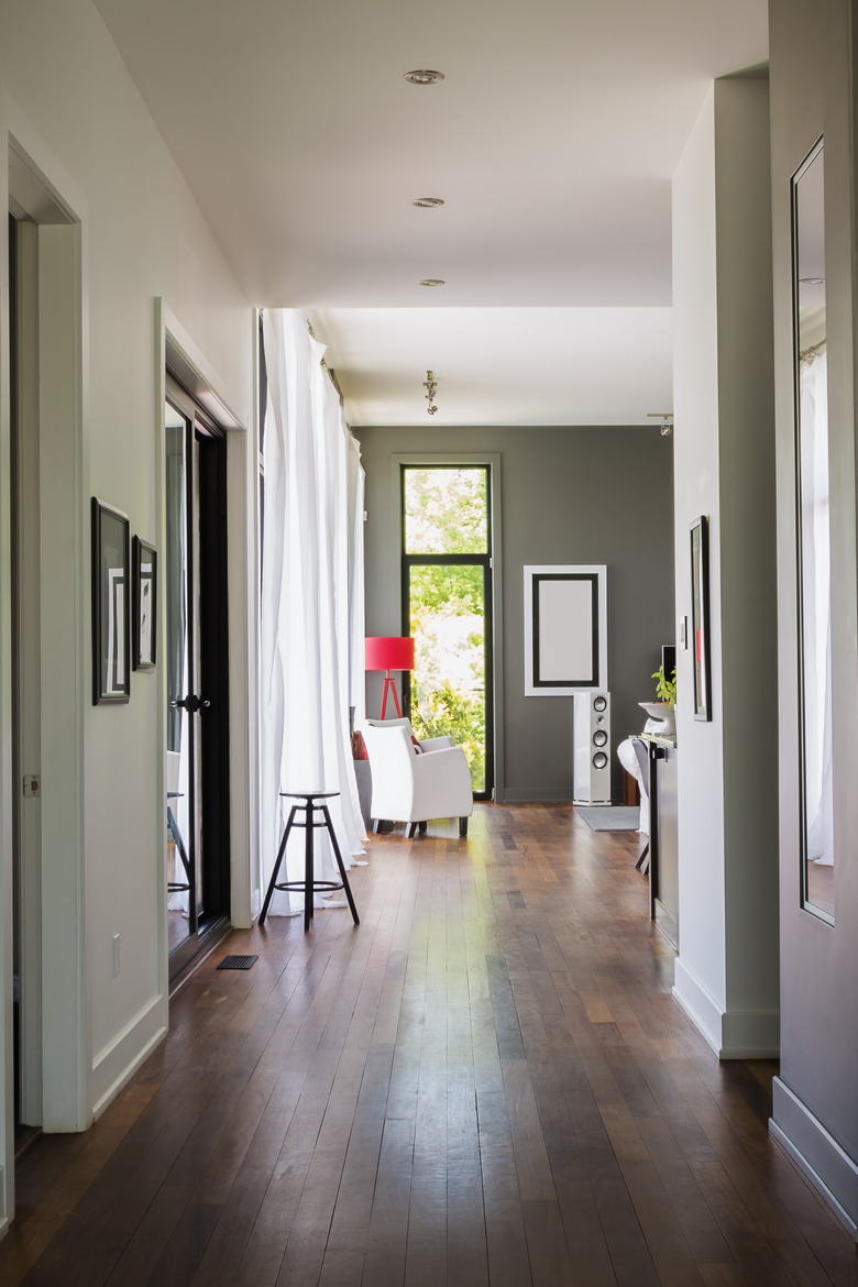 Hallway with qumaru wood floorboards.s leading to living room with white leather armchair, luxurious modern cube style house interior