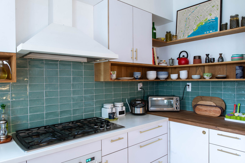 kitchen with blue tile backsplash, white cabitnets, white range hood and stove top