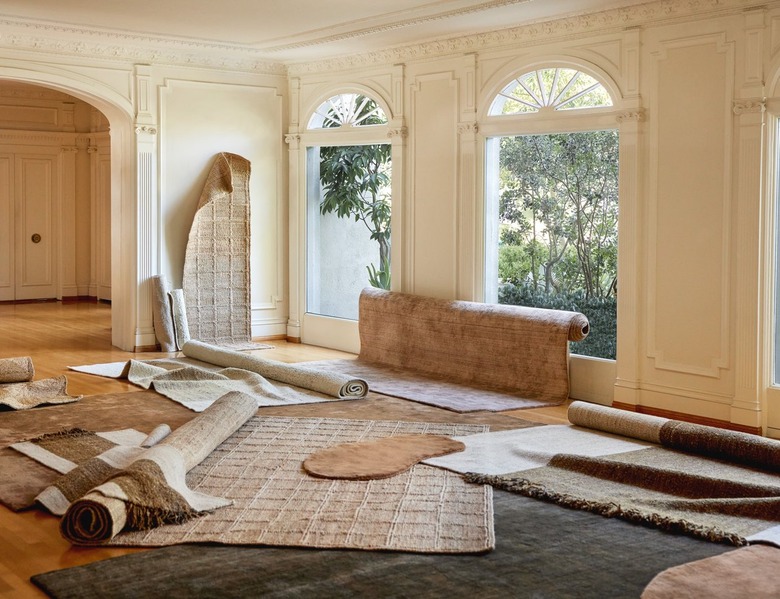 Various neutral-colored rugs scattered around a living room with two large windows.