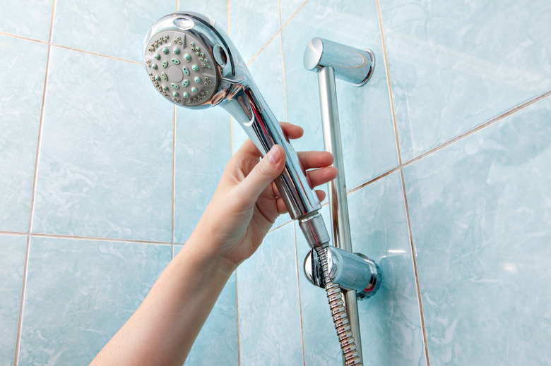 Close-up of human hand adjusts holder shower head with hose.