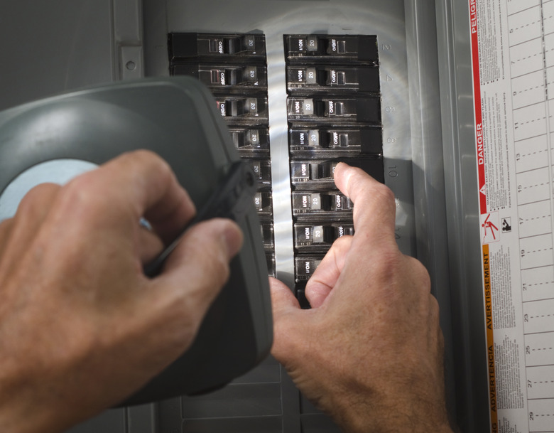 Man with flashlight at residential circuit breaker panel.