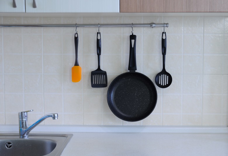 Frying pan with non-stick coating, a spatula for a steak, a spoon against the background of a tiled wall. The interior of the kitchen.