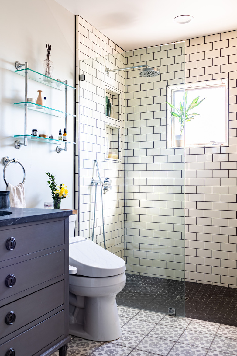 bathroom shower with white subway tile, blue bathroom vanity with sink, toilet and over-the-toilet storage