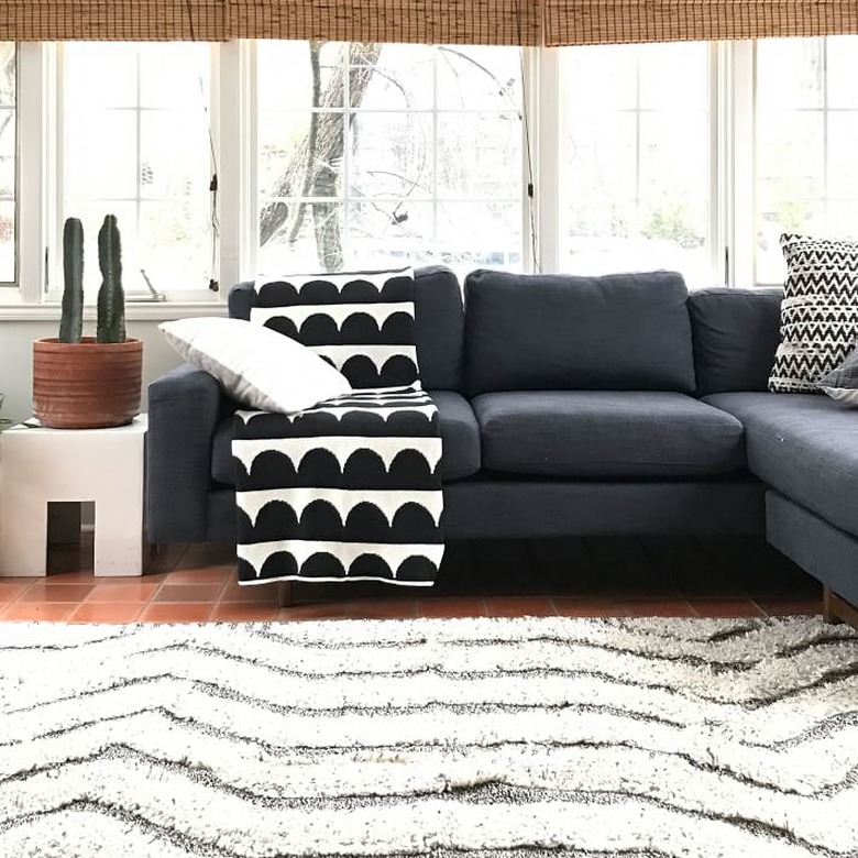 living room with dark couch and white rug and black and white blanket on top of the couch