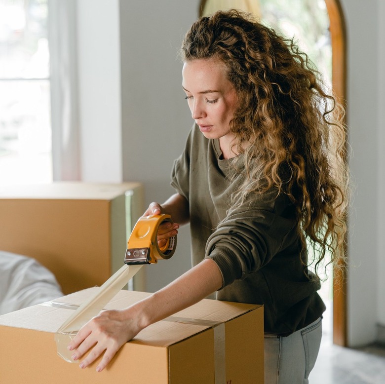 woman closing brown moving box with tape