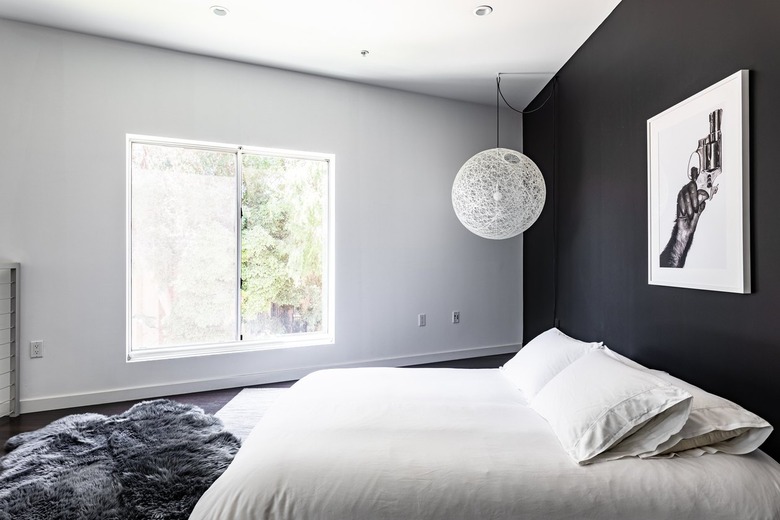 Minimalist bedroom with a black accent wall, string globe pendant light, gray fur rug, and photo art