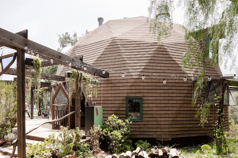 A brown dome-shaped home with a lush garden and string lights strung off the pergola