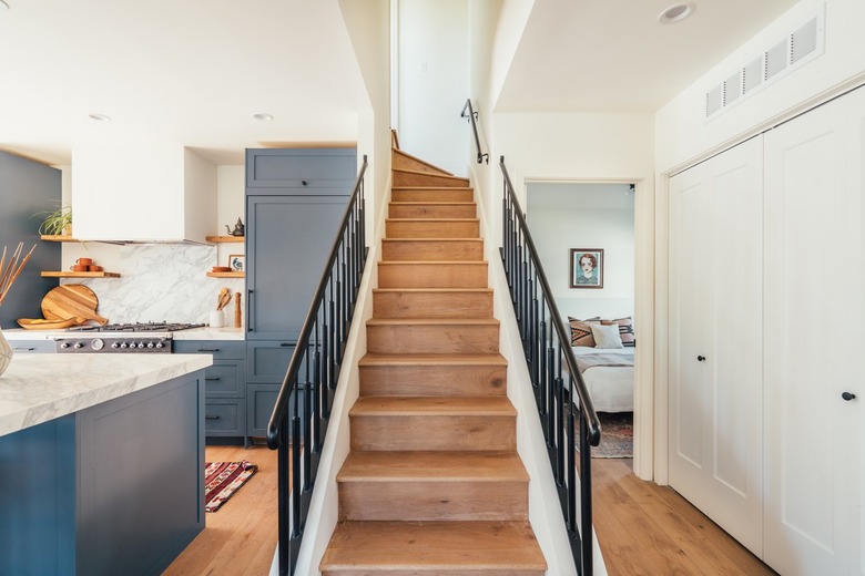 Stairway with wood floor and black rails next to kitchen with blue cabinets and marble countertops