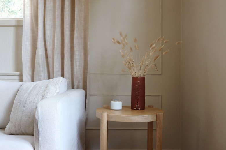 taupe wall with wall moldings inside a room with a couch and table styled with dried flowers