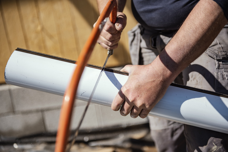 Roofer cutting roof gutter with hand saw.