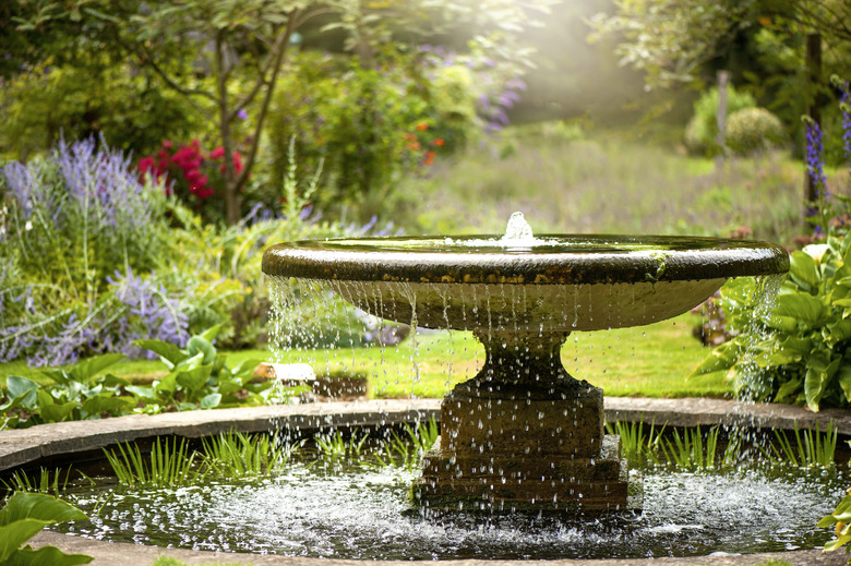 Beautiful summer garden with water fountain in amongst the flowers, in the hazy sunshine