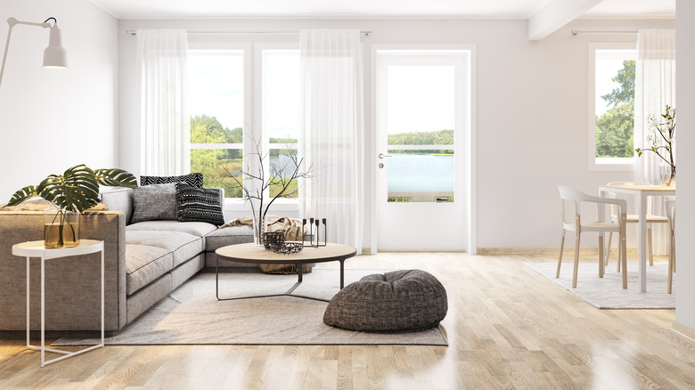 White and beige living/dining room with view of lake through large white-curtained windows.