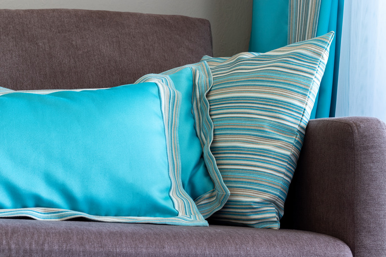 Bright blue designer pillows on a plain brown sofa by the window, interior details closeup