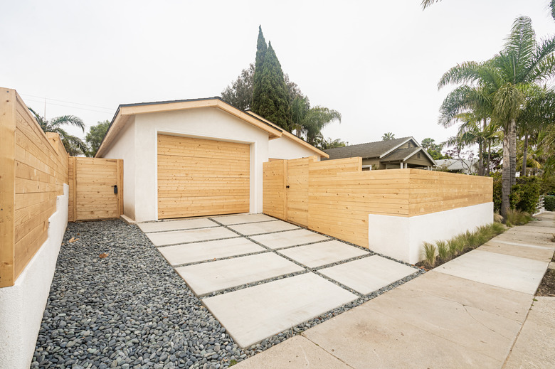 a concrete path surrounded by gravel, a light horizontal fence frames a garage