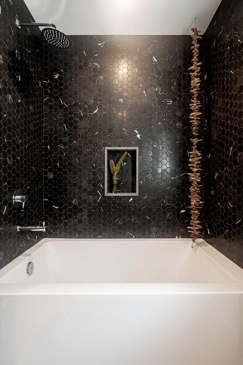 white bath/shower combination, black hexagon tile with white dashes, hanging wooden decoration