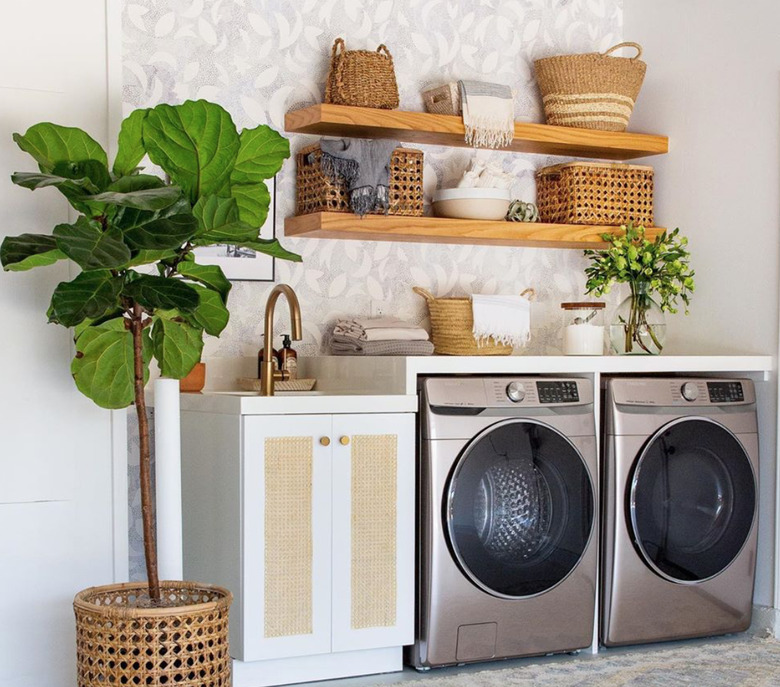 Garage Laundry Room with Stainless steel front load washer dryer, shelf, sink, open natural wood floating shelves, fiddle leaf fig, baskets.