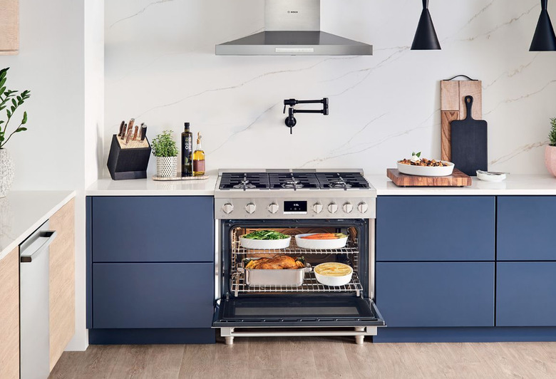 Freestanding Stainless Steel Gas Stove, pot filler, stainless hood, blue cabinets, white marble backsplash.