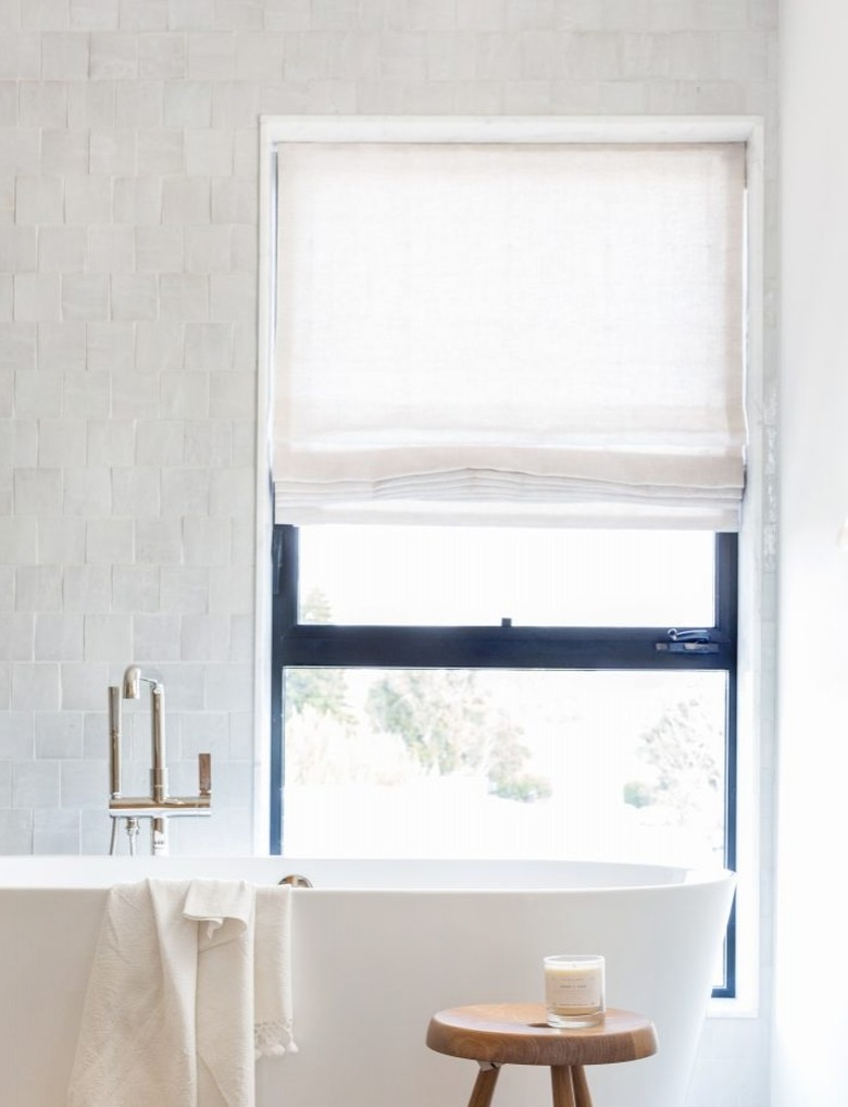 bathroom tub backsplash idea with zellige tile behind freestanding tub and window with Roman shade