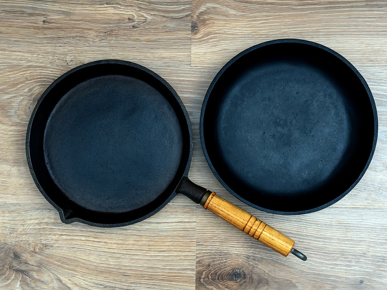 Two cast-iron skillets, one with a wooden handle, on a wood or laminate surface