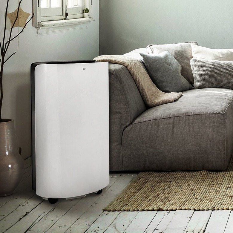 A white portable A/C in a living room with a gray couch and light wood floors