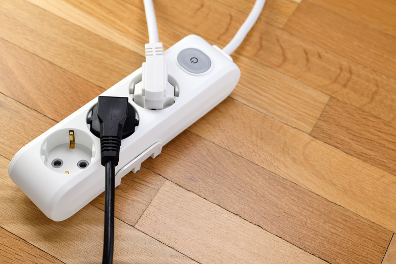 White power strip with three outlets on wooden floor. Power strip with switch for home or office.