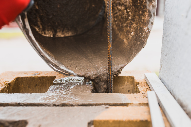 Cement slurry pouring from a bucket into the cells of a concrete block.