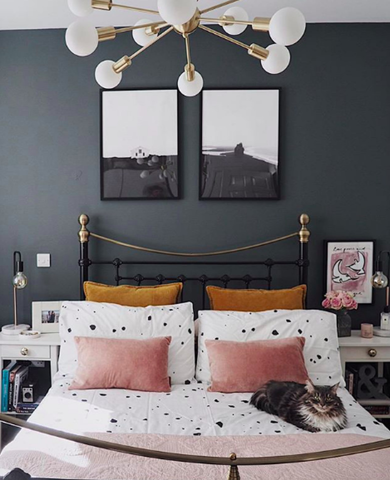 Gray bedroom with white sheets featuring black dot paint spatter and blush and goldenrod velvet pillows. Also featuring brass white globe sputnik chandelier