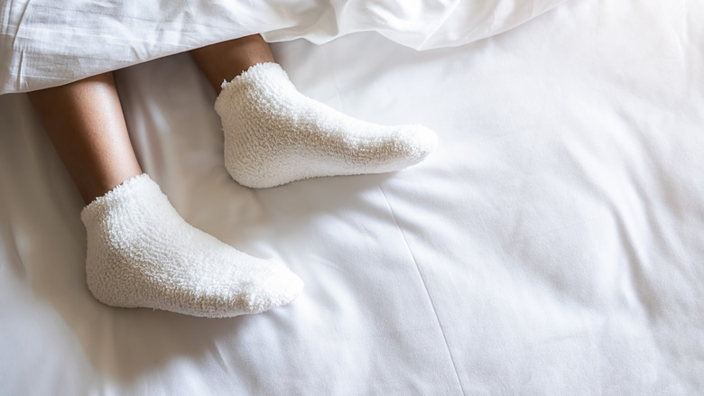 Low Section Of Woman Wearing Sock Relaxing On Bed