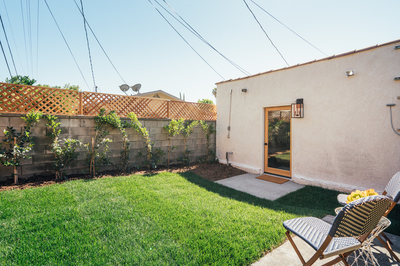 Spanish-style home with a green, freshly mowed yard; a concrete block fence and a blue patio chair are seen in the pho