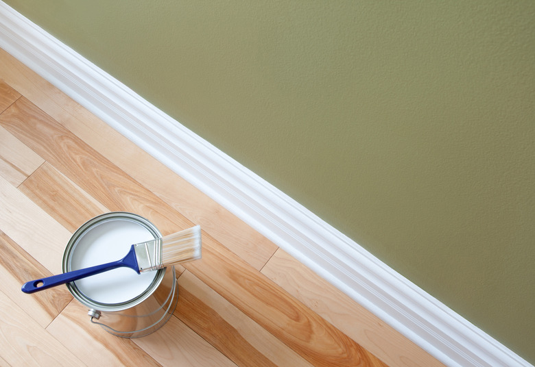 Paintbrush and a can of white paint on wooden floor