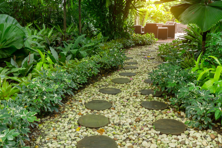 Circle shape of pattern walkway stepping sand stone on white gravel in a backyard garden of lush greenery plant, shrub and trees