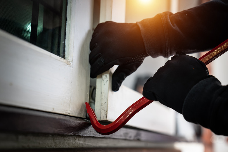 dangerous masked burglar with crowbar breaking into a victim