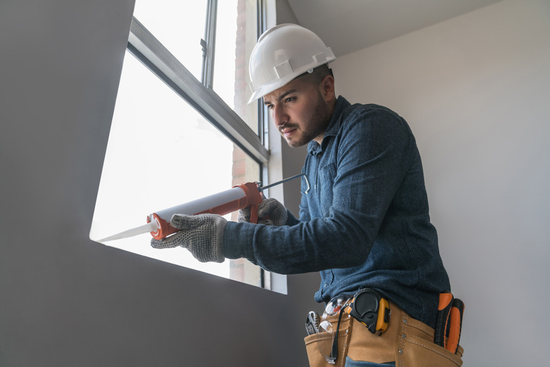 Building contractor installing a window and applying silicone sealant