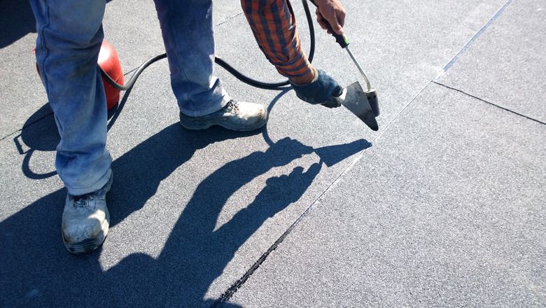 Roofer preparing part of bitumen roofing felt roll for melting by gas heater torch flame