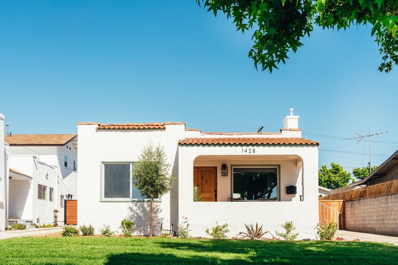 A front lawn of a Spanish style white house with terra-cotta roof tiles