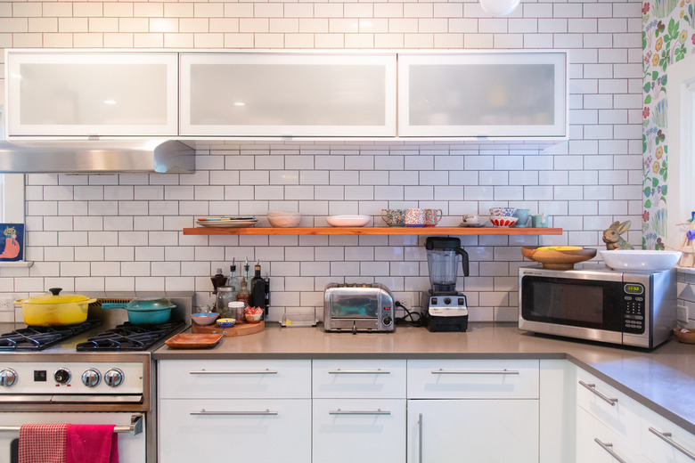 kitchen with subway tile wall, white kitchen cabinets and appliances on the countertop