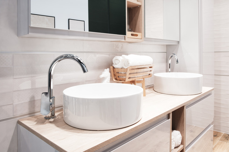 Two luxury faucet mixer on a round bowl white sink in a beautiful beige gray bathroom